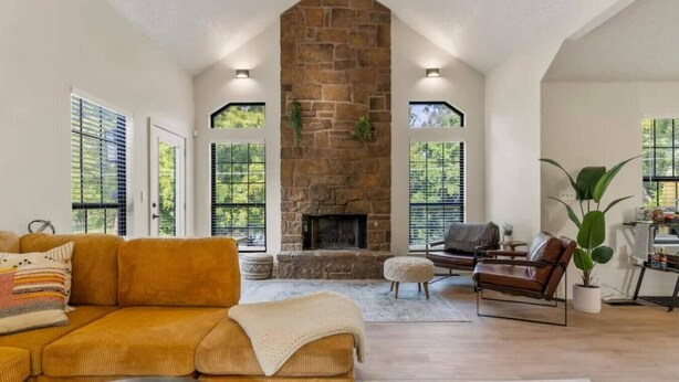 Amplia sala de estar con chimenea de piedra, asientos cómodos y ventanas grandes.