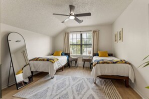 A bedroom with two beds, a ceiling fan, a window with curtains, a desk, and a mirror. - Turkey Mountain Trailside by Tulsa Getaways (Tulsa)