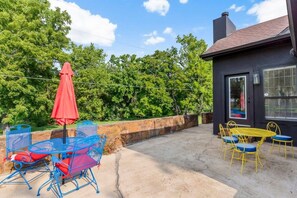 An outdoor patio with metal chairs and tables, a red umbrella, and a stone wall.