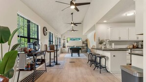 Una cocina amplia con una isla central, taburetes de bar y una zona de comedor con mesa de billar.