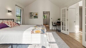 Un dormitorio con una cama grande, un escritorio y una silla, con vista a un jardín a través de la ventana.
