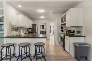 A modern kitchen with white cabinetry, a central island with stools, a built-in oven, and a trash bin. - Turkey Mountain Trailside by Tulsa Getaways (Tulsa)