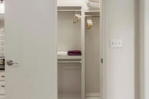 Ein weißer Kleiderschrank mit hängender Kleidung und einem Regal für gefaltete Kleidung.
