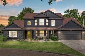 A two-story house with a dark exterior, a front porch with seating, and a garage.