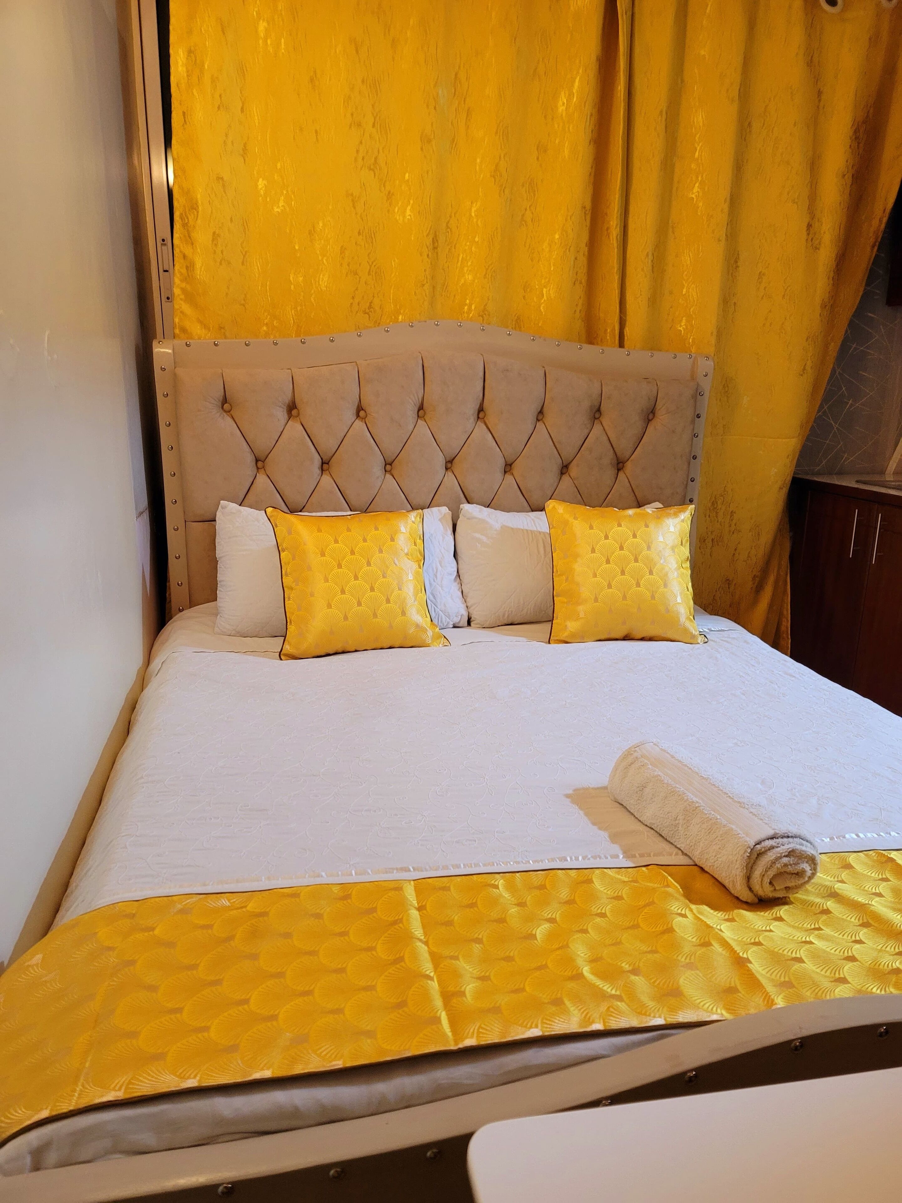 A neatly made bed with a tufted headboard, two pillows, and a rolled towel.