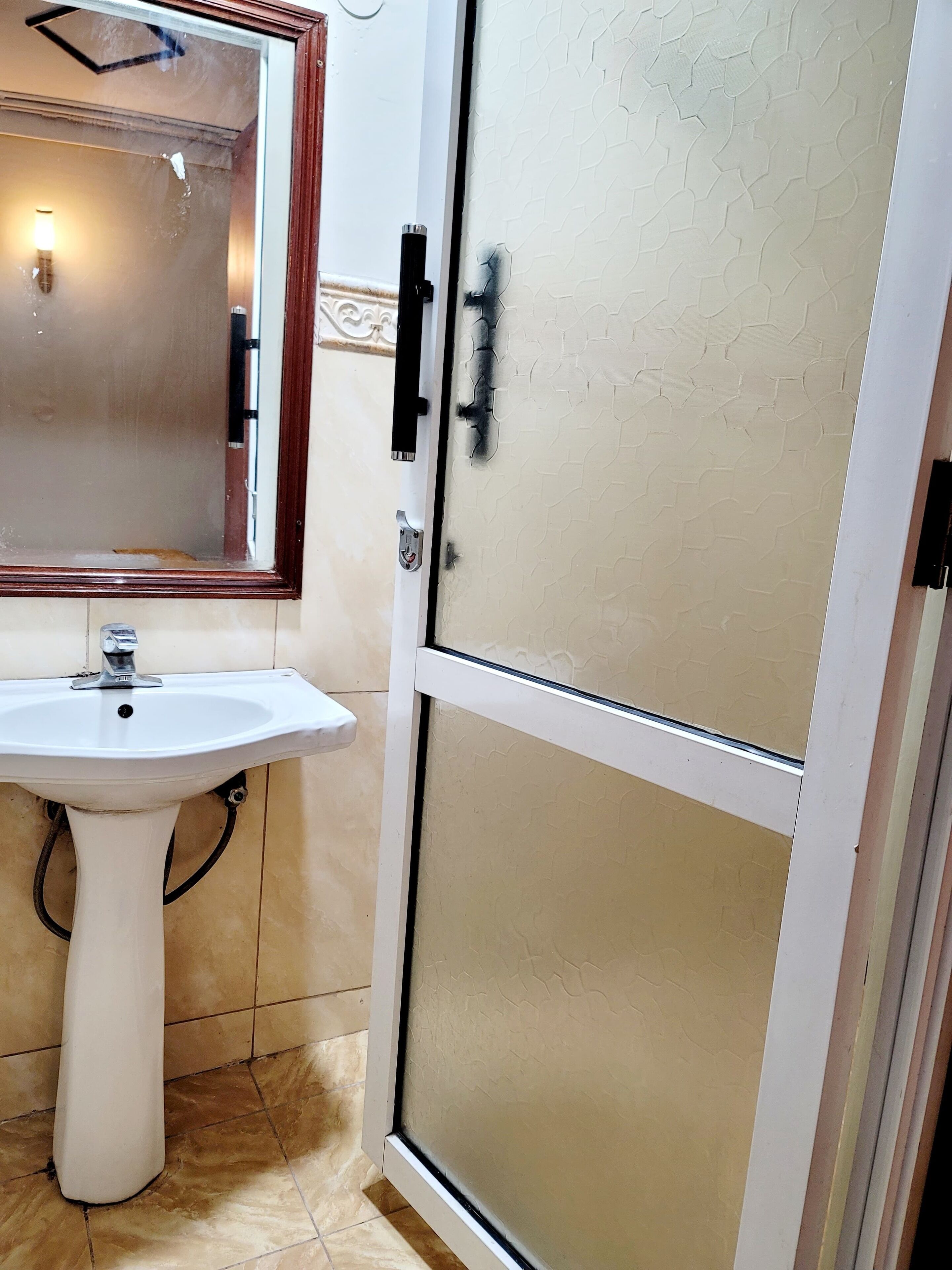 A bathroom with a pedestal sink, a mirror, and a frosted glass shower enclosure.