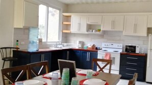 A modern kitchen with white cabinets, a stove, and a refrigerator. There is a dining table set with plates and glasses. - Nice and Cozy for 6 in Pastores Antigua Guatemala, 8 min from downton Antigua  (Pastores)