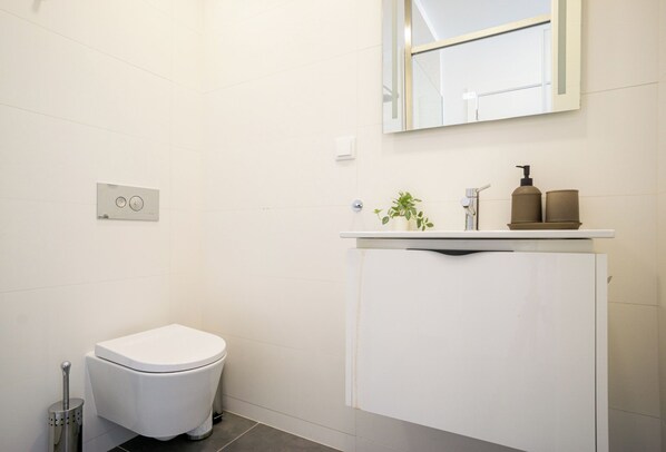 Une salle de bain avec des toilettes, un lavabo avec un miroir au-dessus et une petite plante posée sur le comptoir.