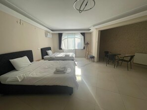 A hotel room with two beds, a small table with chairs, a radiator, and a window with curtains. - Blue Life Hotel (Izmir)
