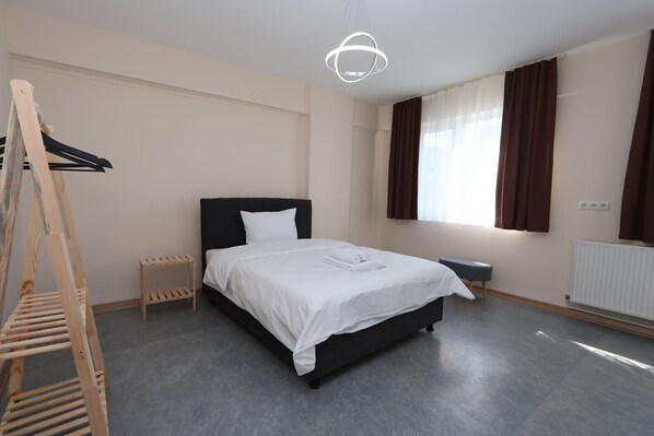 Een moderne hotelkamer met een groot bed, een houten ladder, een klein bijzettafeltje en een raam met gordijnen.