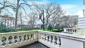 A balcony with a balustrade overlooking a park with trees and buildings. - Upscale Urban Haven: Luxury Flat (London)