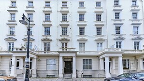 A multi-story building with a symmetrical facade, evenly spaced windows, and a central entrance with a black door. - Upscale Urban Haven: Luxury Flat (London)