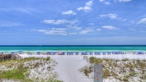 A beach with a clear sky, a sandy path leading to the water, and several umbrellas. - Sapphire by the Sea (Miramar Beach)