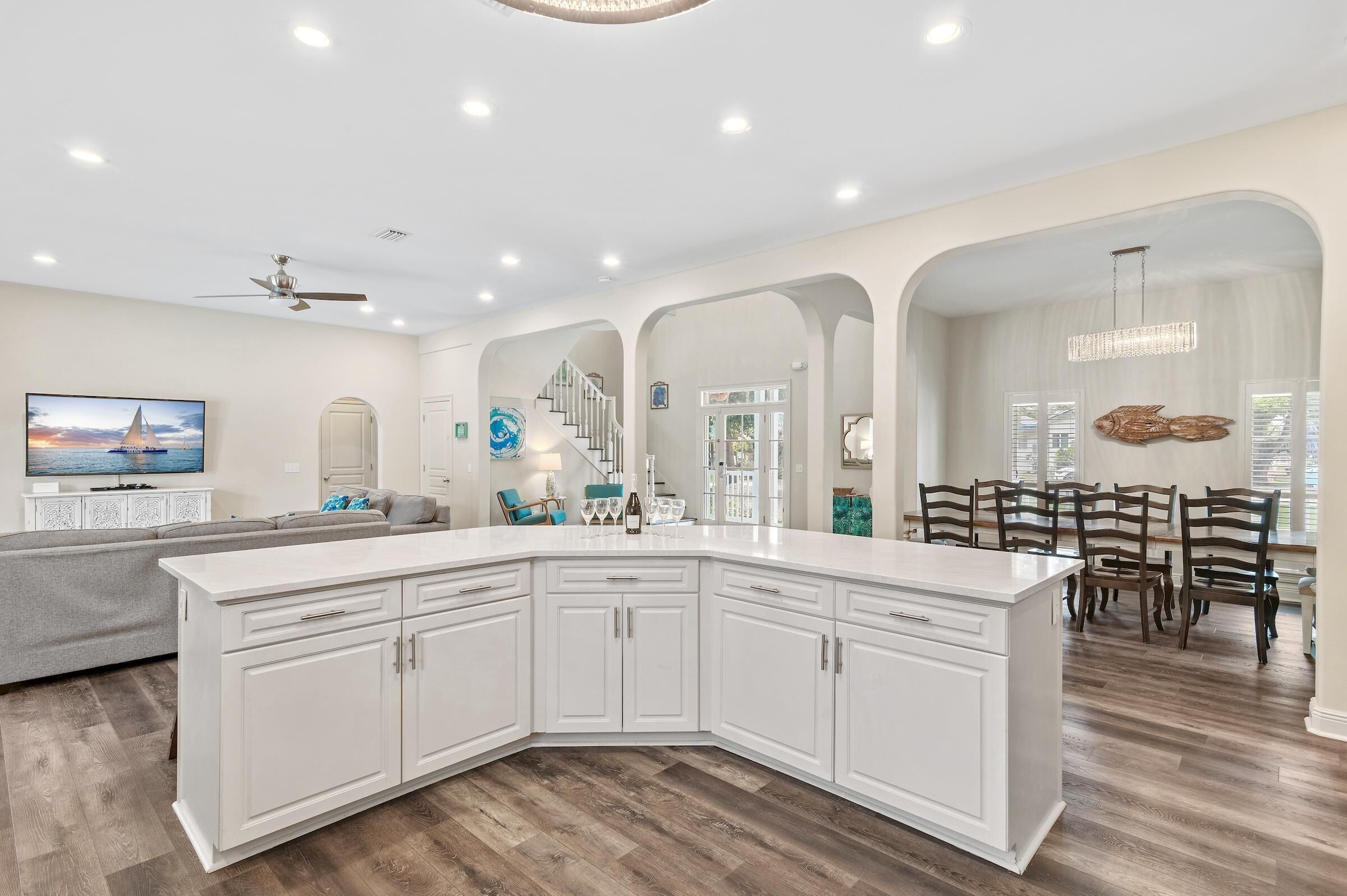 A modern kitchen with white cabinetry, a large island, and a dining area with wooden chairs.