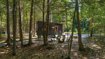 A cabin surrounded by trees with a picnic table and chairs.