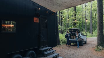 Ein rustikales Blockhaus mit überdachter Veranda, ein geparktes Auto in der Nähe und ein Feldweg, der durch einen Wald führt.