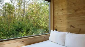 A bedroom with a wooden ceiling, a large window, and a bed with white bedding.