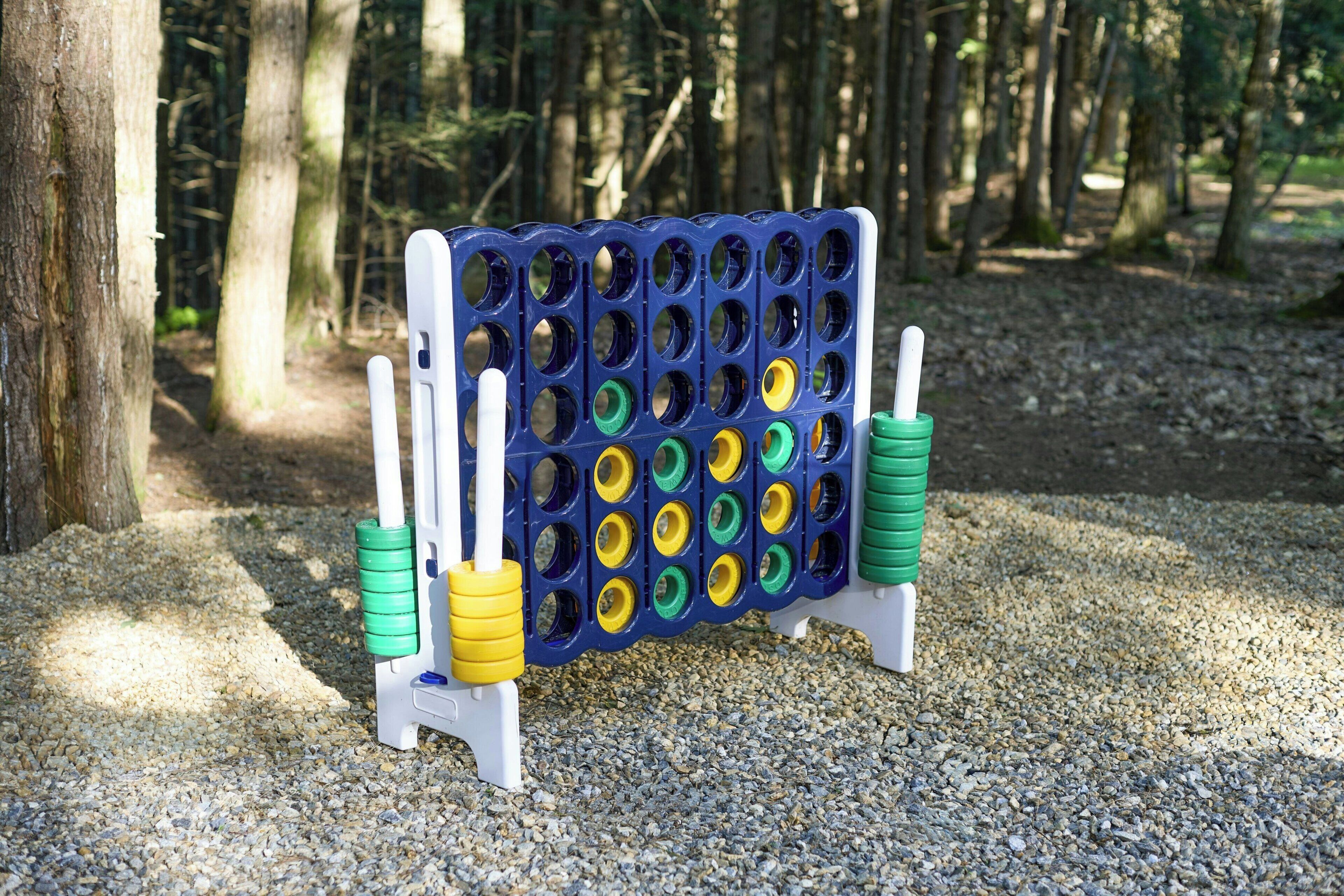 Een prikbord met meerdere gaten, ondersteund door witte steunen, geplaatst op een grindpad in een bebost gebied.