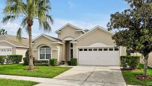 Ein Wohnhaus mit Garage, Auffahrt und gepflegter Bepflanzung, darunter ein Palmenbaum und Büsche.