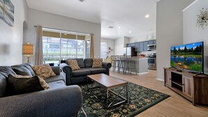 Ein modernes Wohnzimmer mit Sofa, Couchtisch und Fernseher, verbunden mit einer Küche mit Bar und Essbereich.