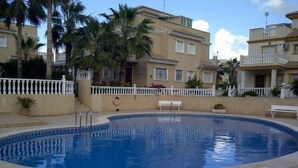 A swimming pool surrounded by a white fence, with a building in the background. - Immaculate and Spacious Playa Flamenca Townhouse LONG TERM REDUCED RENTAL RATES (VC)