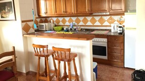 A kitchen with wooden cabinets, a microwave, a kettle, and a sink. There are two wooden chairs and a small island with a countertop. - Immaculate and Spacious Playa Flamenca Townhouse LONG TERM REDUCED RENTAL RATES (VC)