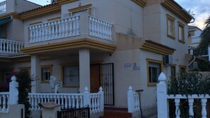 A two-story residential building with a balcony, a gated entrance, and a visible address sign. - Immaculate and Spacious Playa Flamenca Townhouse LONG TERM REDUCED RENTAL RATES (VC)
