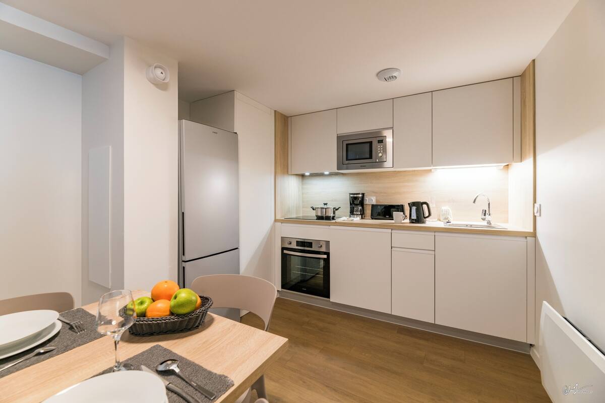 Cozinha moderna com armários brancos, micro-ondas, forno e um espaço de refeições com mesa posta para dois.