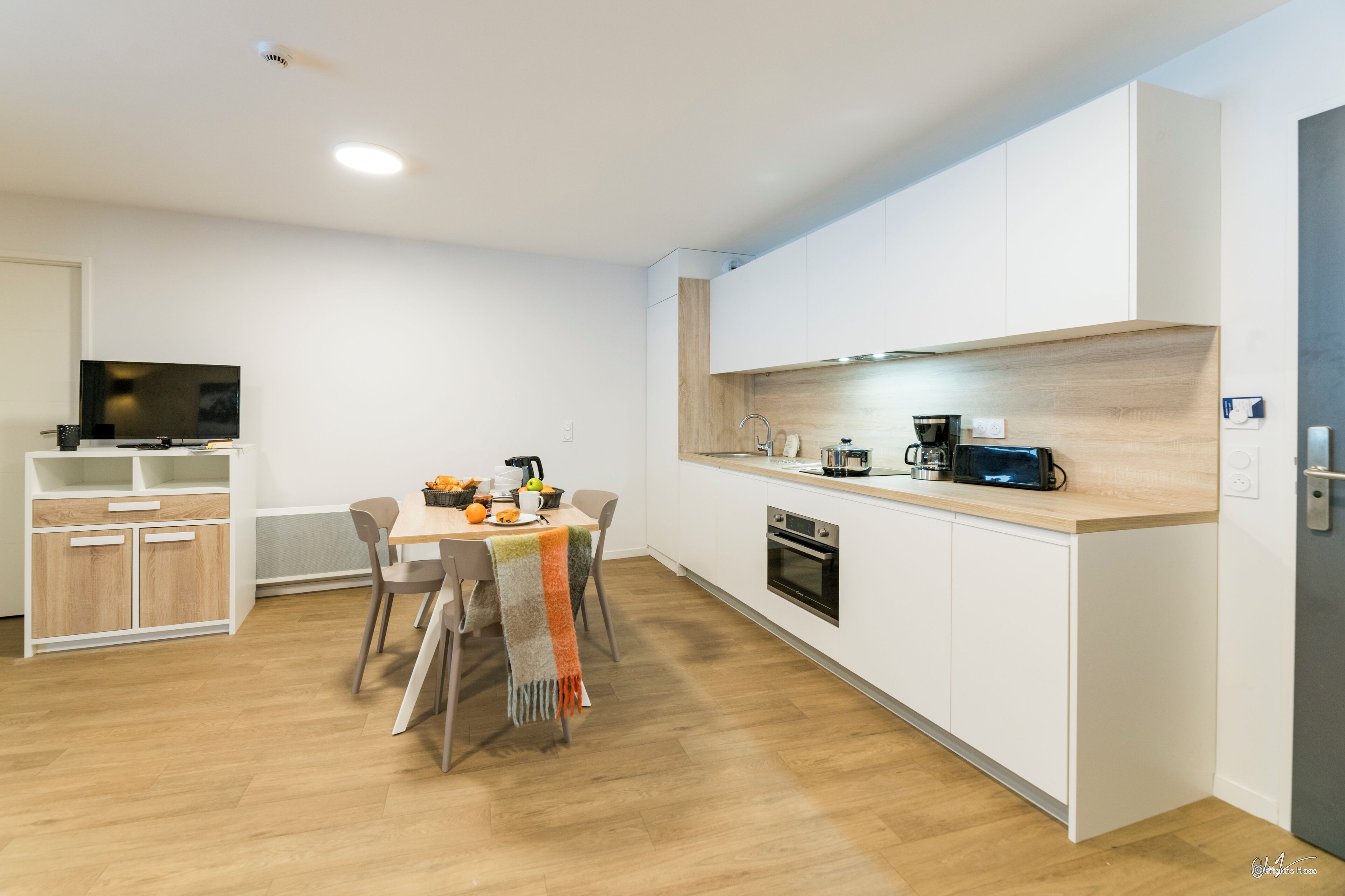 Une cuisine moderne avec des meubles blancs, un plan de travail en bois et un coin repas comprenant une table et des chaises.