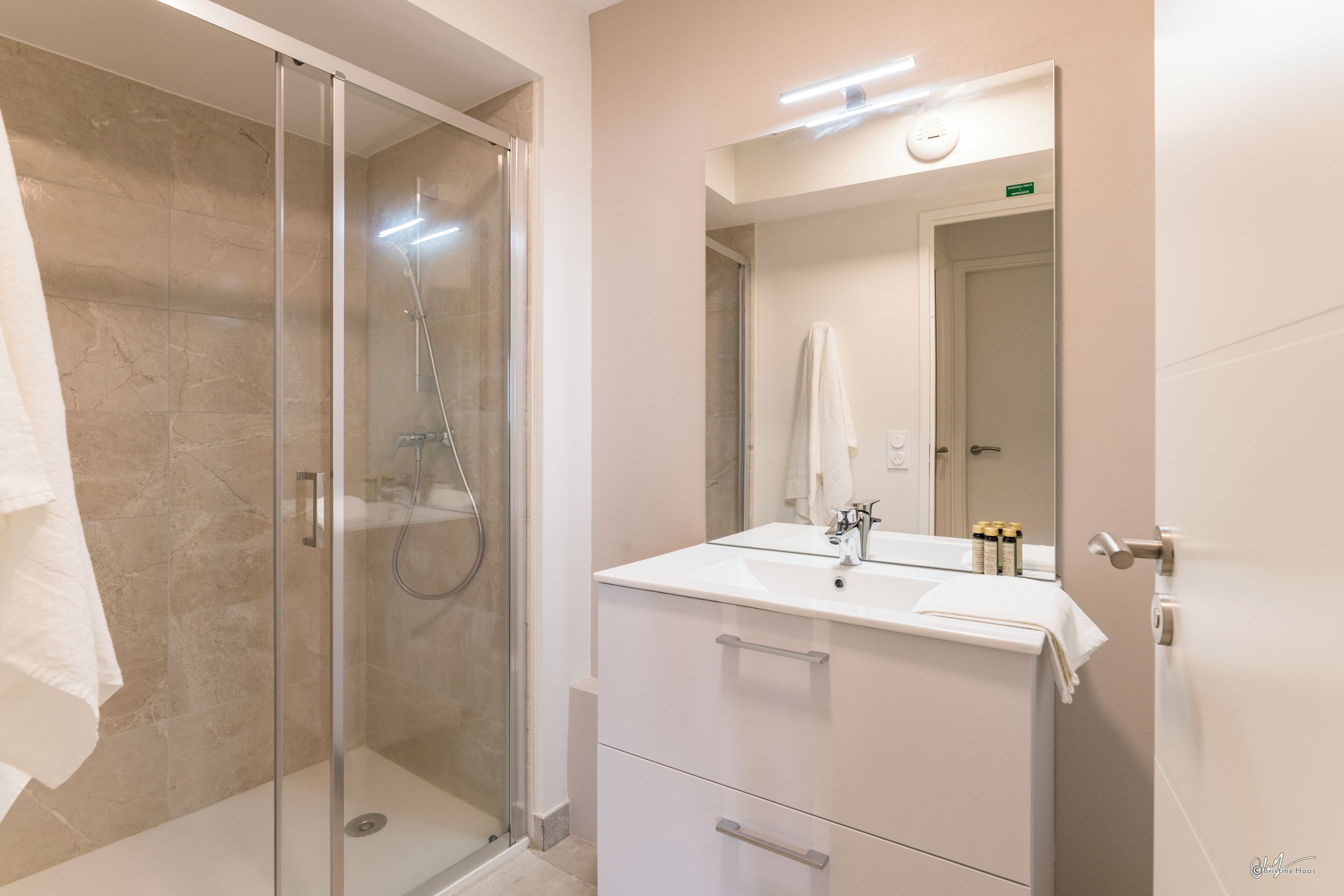 Uma casa de banho moderna com cabine de duche em vidro, lavatório branco com espelho e porta com uma toalha pendurada.