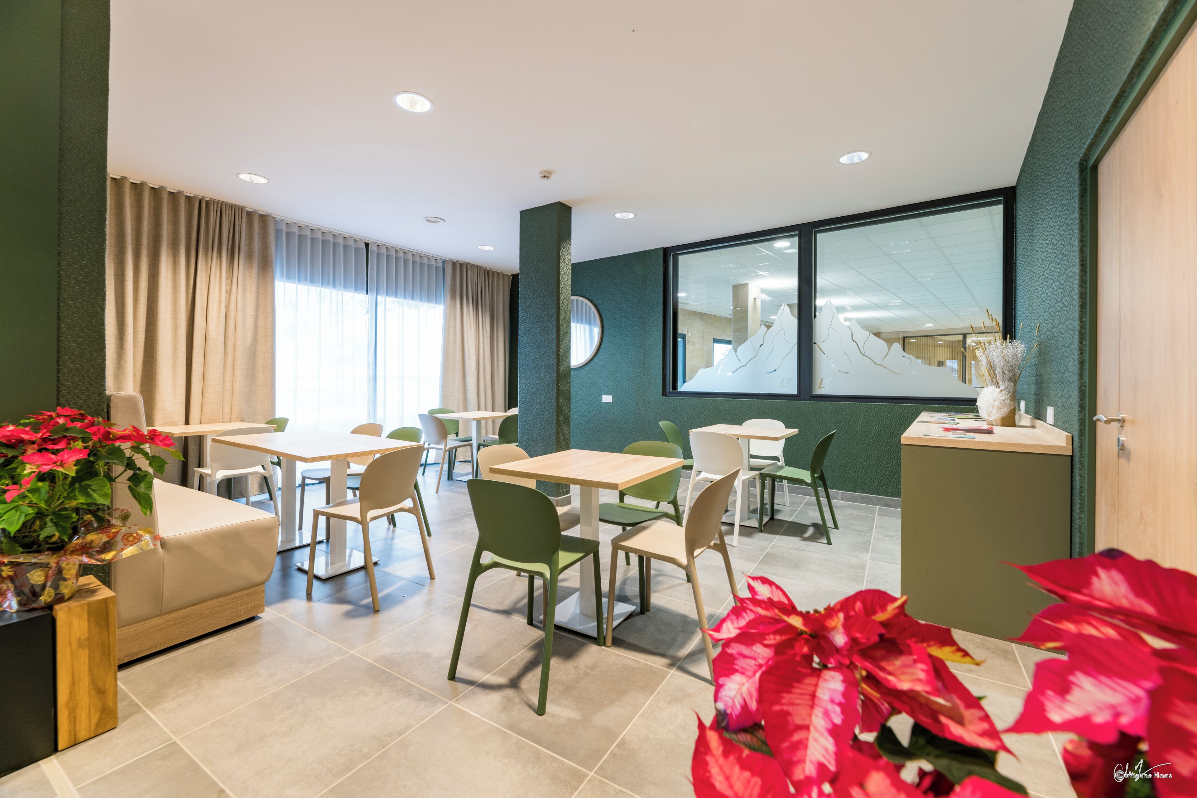 A modern dining area with tables and chairs, a sofa, and a large window with a view.
