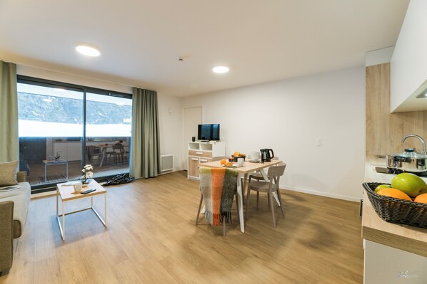 A modern living room with a dining area, a kitchen, and a large window with a view.