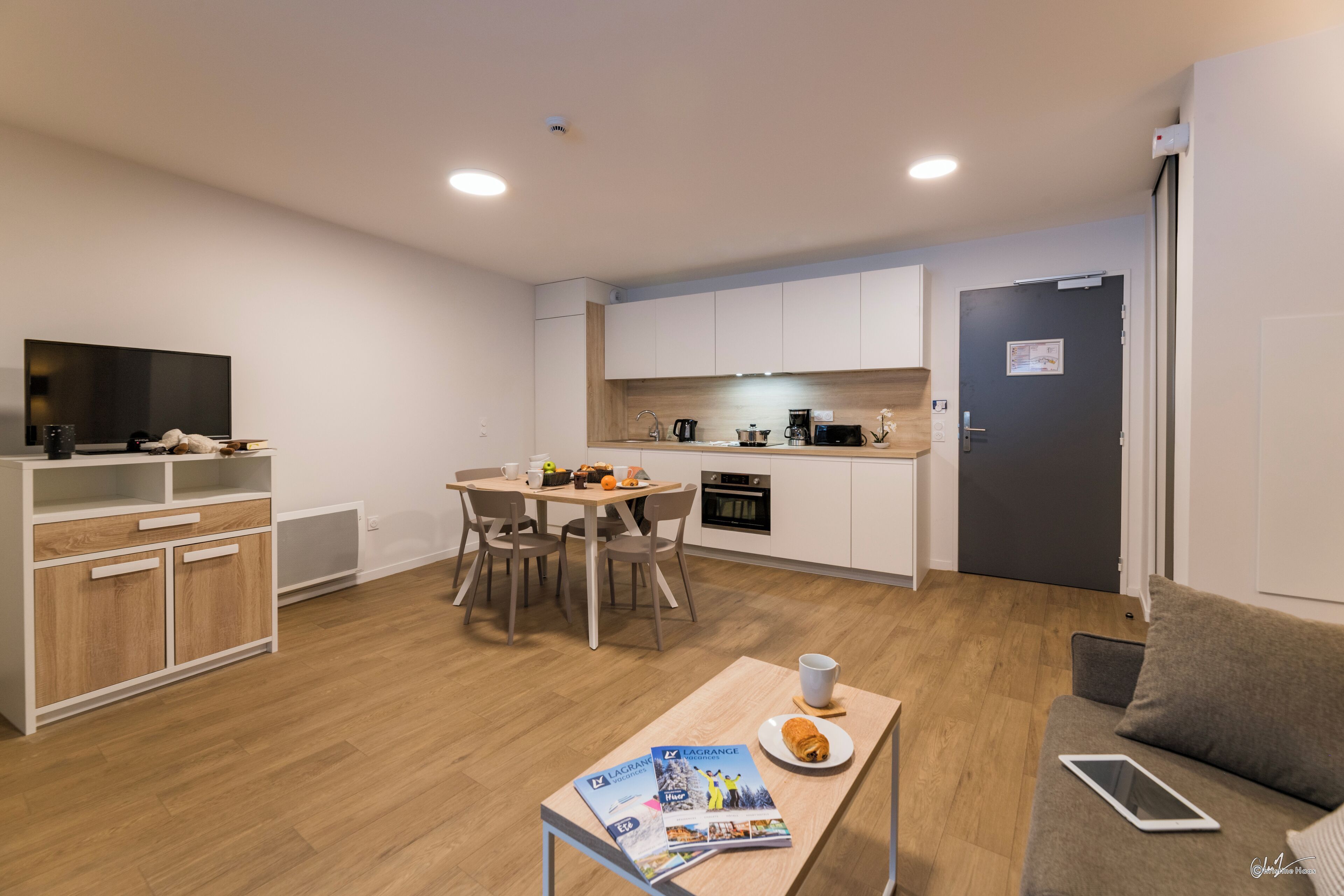 A compact living space with a dining area, kitchenette, and a sofa with a tablet.