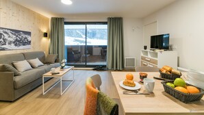 A modern living room with a sofa, a coffee table, a TV, and a dining area with a table set for breakfast. - Lagrange Vacances Le Cristal de Piau  (Aragnouet)