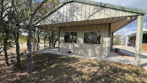 A modern building with a covered patio area, large windows, and a concrete pathway leading to it. - Captain's Cabin on Lake Godstone (Graford)