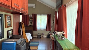 A compact, well-lit room with wooden cabinets, a bed, a desk with a printer, a window with curtains, and a small table with a drone model. - Captain's Cabin on Lake Godstone (Graford)