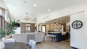 A modern kitchen with a central island, a dining area with a round table, and a living room with a sofa and a large plant.