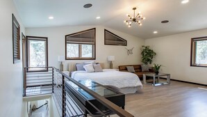 A spacious bedroom with a large bed, a glass desk, a sofa, and a ceiling light fixture.