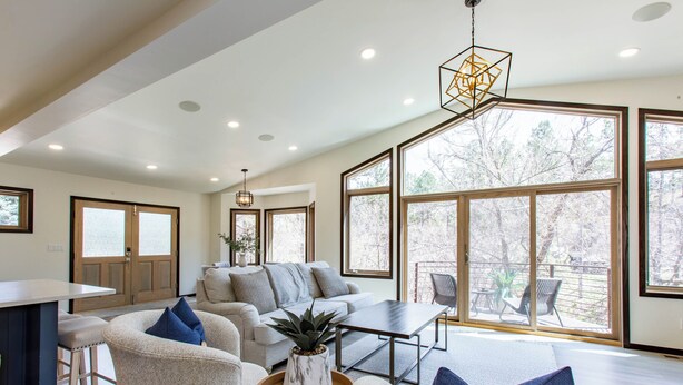 A spacious living room with a sofa, chairs, a coffee table, and a dining area. Large windows provide natural light and views of the outdoors.