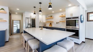 A modern kitchen with a large island, bar stools, stainless steel appliances, and pendant lighting.