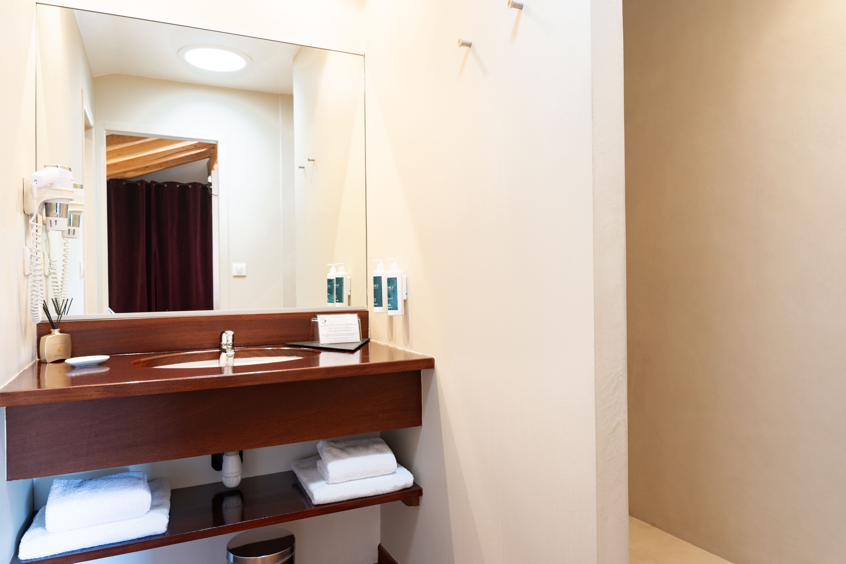 Une salle de bain avec un meuble-lavabo en bois, un miroir, un porte-serviettes et un sèche-cheveux.