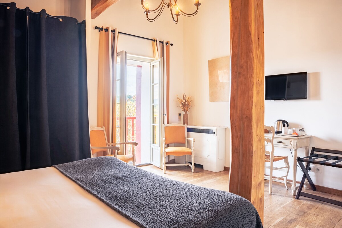 A hotel room with a bed, a desk, and a chair. There is a television on the wall and a window with curtains.