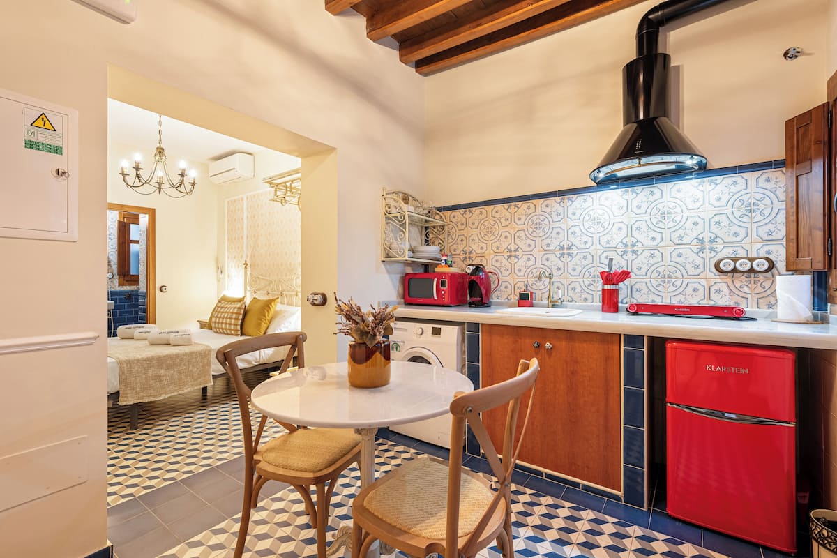 A compact kitchen with a red refrigerator, a microwave, and a sink. There is a dining table with chairs and a chandelier.