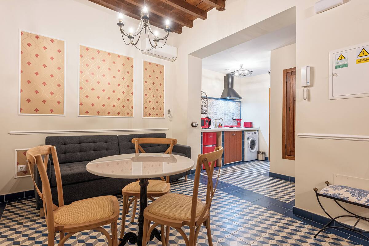 A dining area with a round table and four chairs, a sofa, and a chandelier.