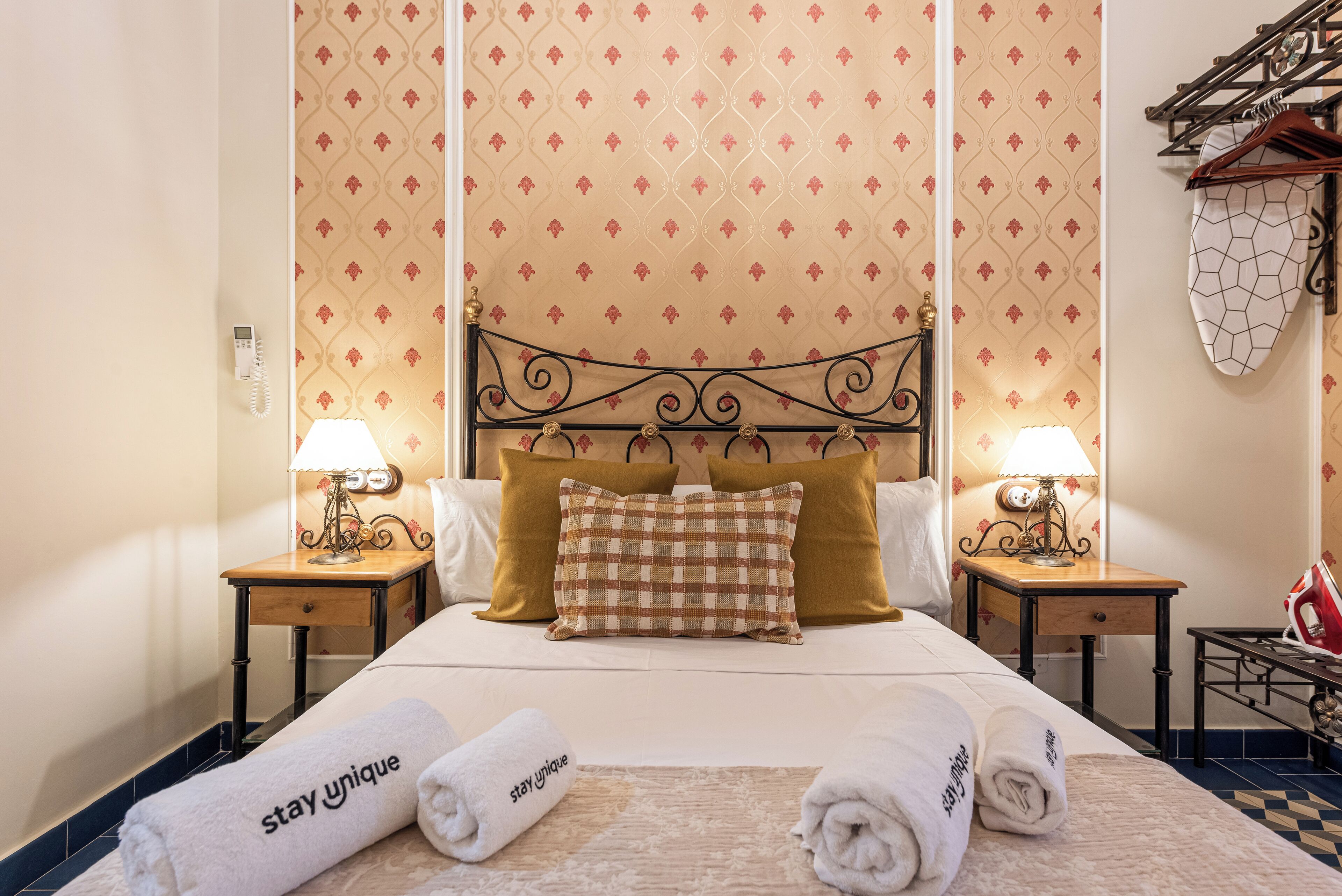 A hotel room with a bed, two bedside tables, two lamps, a headboard, and a towel rack.