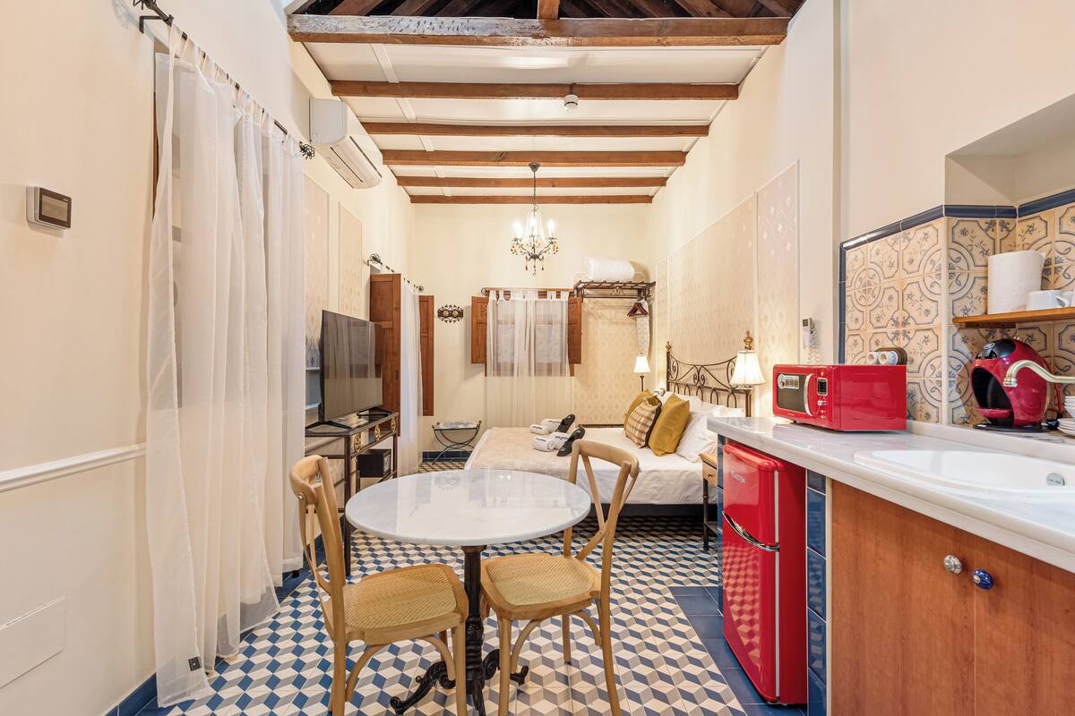 A compact room with a dining table, chairs, a bed, a small kitchenette, and a bathroom.