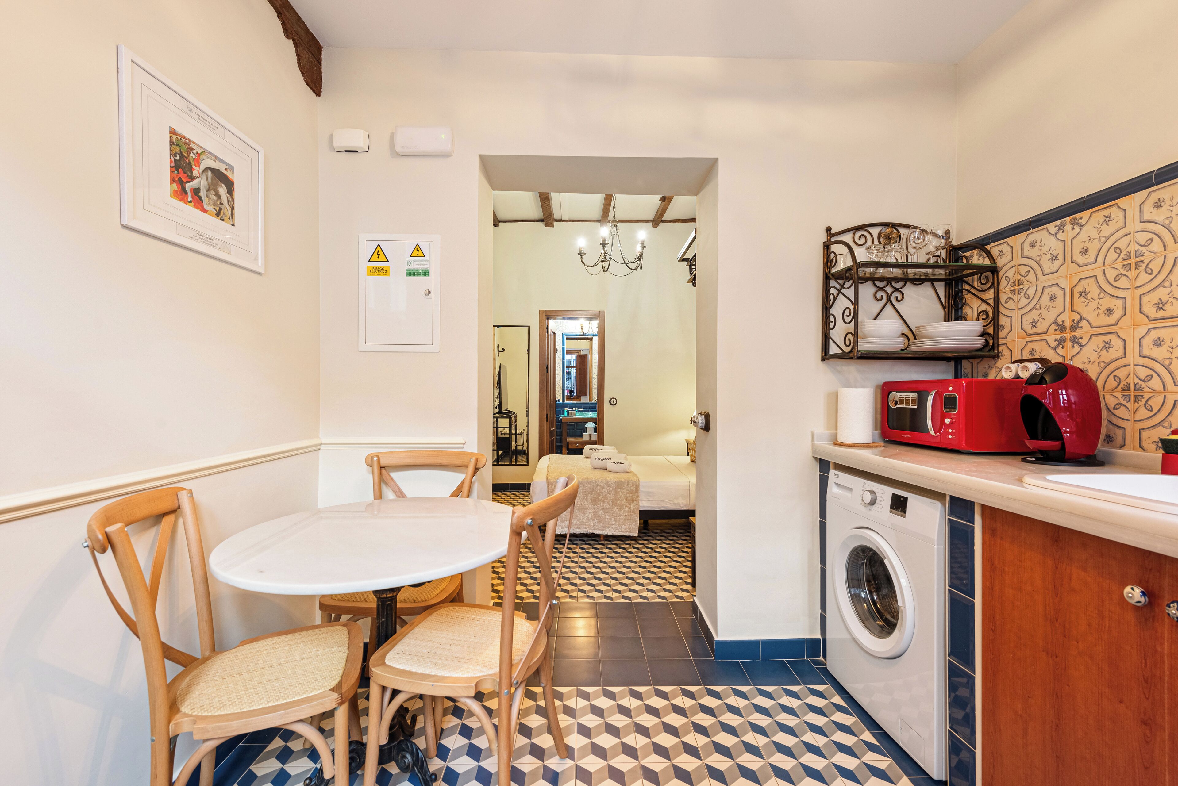A compact kitchen with a washing machine, a dining table with chairs, and a microwave on the counter.