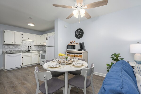 A modern kitchen with white cabinets, a dining table with chairs, a ceiling fan, and a sign that says 'Coffee Bar'.