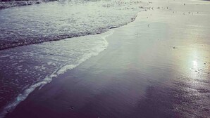 Una playa con un rompeolas rocoso, olas y cielo despejado.