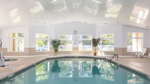 Una piscina interior con paredes de vidrio transparente, plantas en macetas y un reloj en la pared.